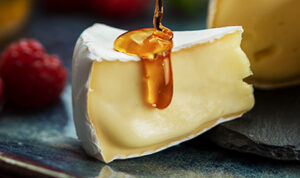 Imagem em close de queijo brie com mel escorrendo representando as soluções para o PDV da Polenghi por Just Trade Marketing